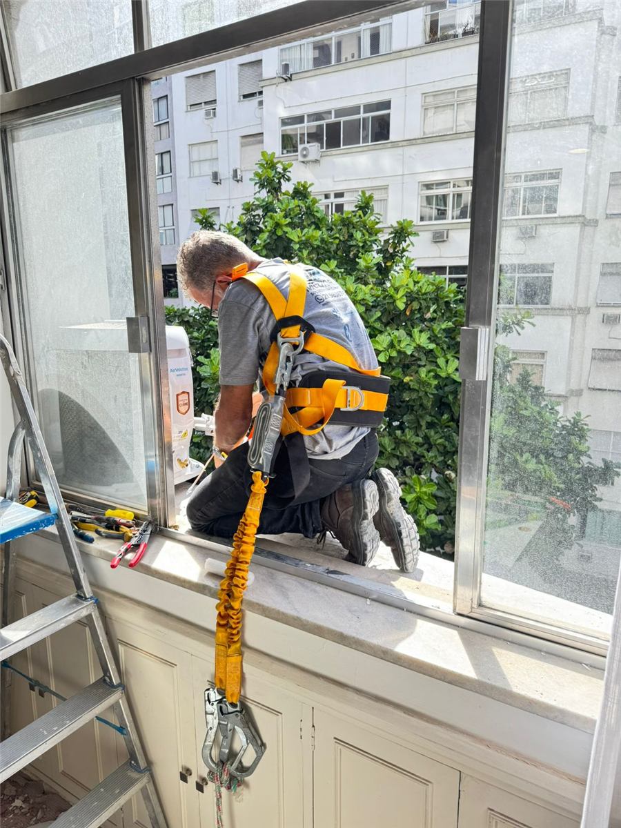 Técnico com cinto de segurança e talabarte instalando condensadora na janela